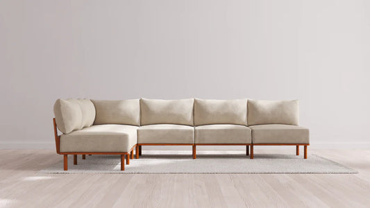The Indoor Jack 6-Seater Open-Ends Corner Sectional in Balsa sits on a light gray rug on a wooden floor against a plain white wall. The sofa is designed with an L-shape, consisting of five connected seats.