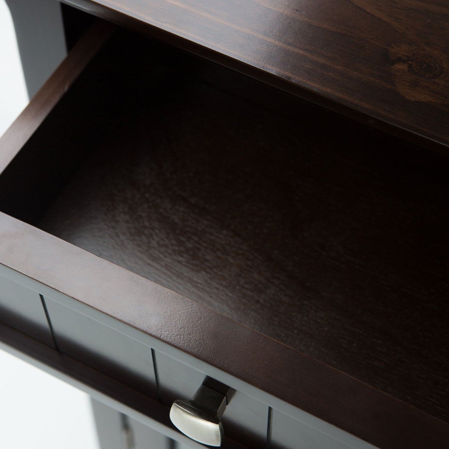 Close-up view of an open, empty Acadian Entryway Storage Cabinet in Brunette Brown with a silver handle, showing its dark interior and part of the top surface.