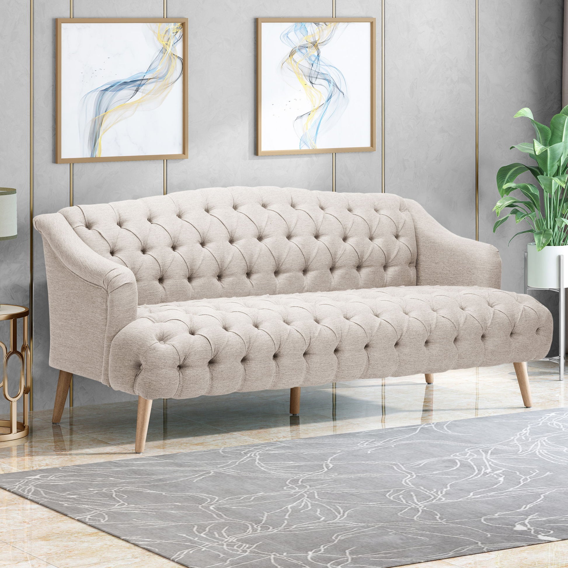 The Comfy 3 Seat Sofa With Wooden Legs, ideal for living rooms and studies, sits on a patterned rug before a gray wall accented by abstract art and a nearby green potted plant.