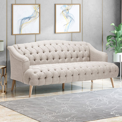 The Comfy 3 Seat Sofa With Wooden Legs, ideal for living rooms and studies, sits on a patterned rug before a gray wall accented by abstract art and a nearby green potted plant.