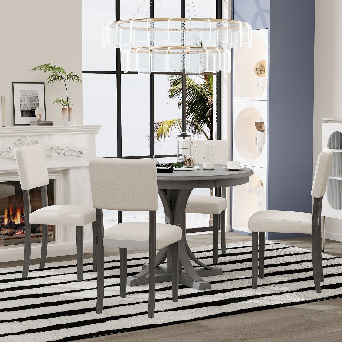 A modern dining room features the Retro Round Dining Table Set with curved trestle legs and upholstered chairs, a striped rug, fireplace, houseplants, and a large window framing palm trees. A contemporary chandelier hangs above.
