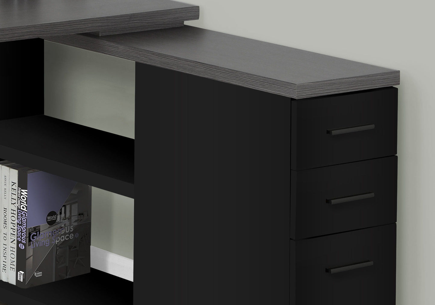 Close-up of a contemporary black L-shaped Computer Desk with storage drawers and a raised shelf, designed for home office use, featuring an open lower shelf with books, set against a light wall.