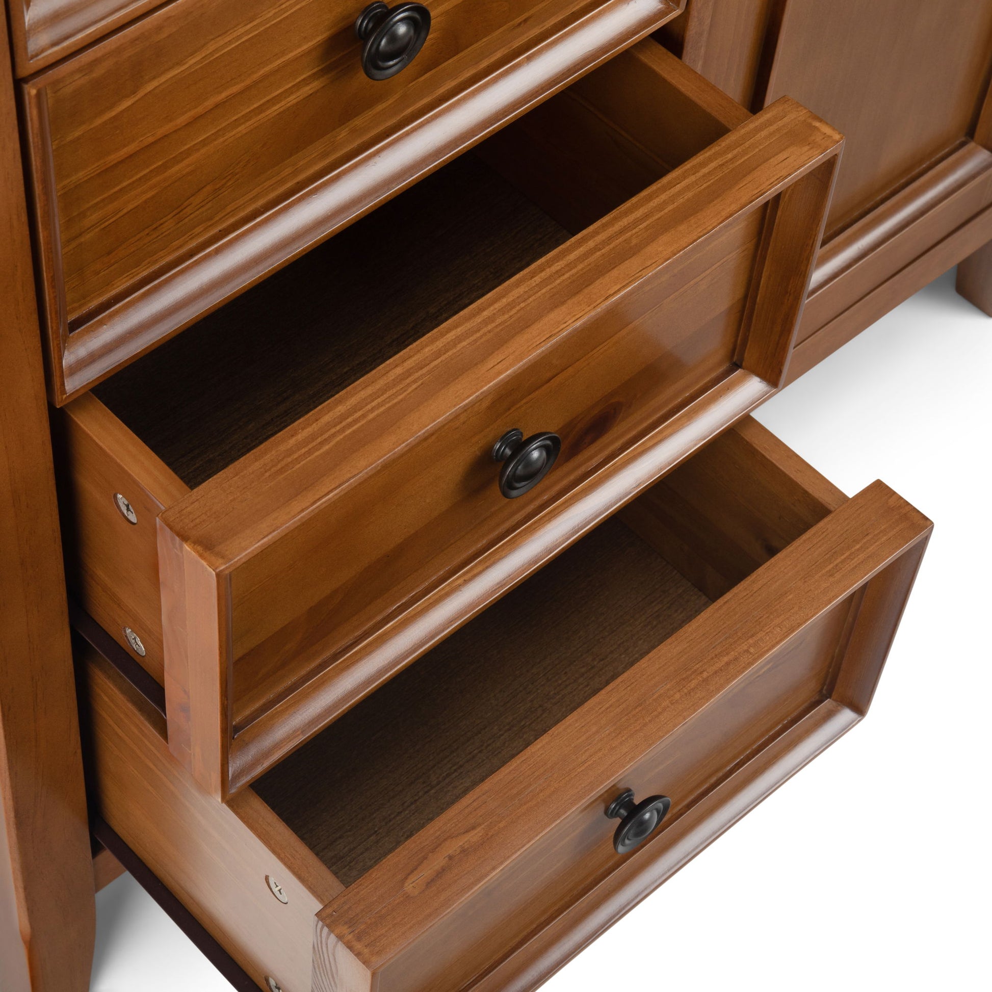 A close-up of the Amherst - Handcrafted Medium Storage Cabinet, featuring three partially open drawers made of smooth brown wood with black round handles.