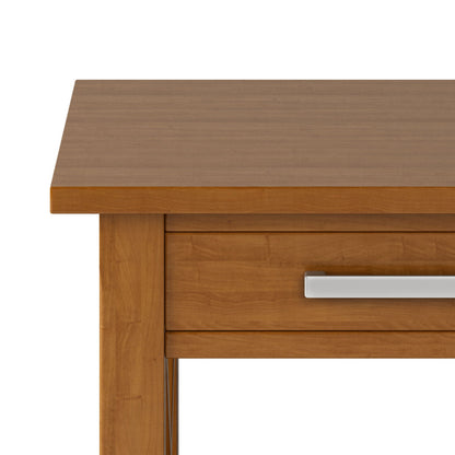 A close-up of the Kitchener - Handcrafted Table shows its warm, medium-brown wood finish, smooth surface, and a drawer with a sleek horizontal silver handle.