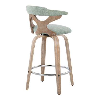 The Gardenia Mid Century Modern Fixed Height Counter Stool (Set of 2) features light wood legs, a curved backrest, and a light green upholstered seat and back, with a metal footrest ring connecting the legs near the base.