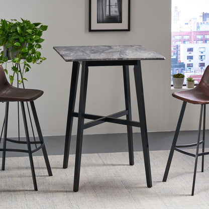 A Modern Bar Height Dining Table with a laminate top and rubberwood legs stands between two brown barstools in a bright room featuring a plant, framed picture, and city view through the window.