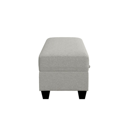 The Drason Storage Ottoman is a rectangular, light gray upholstered piece with black wooden legs, shown from the narrow end against a white background.