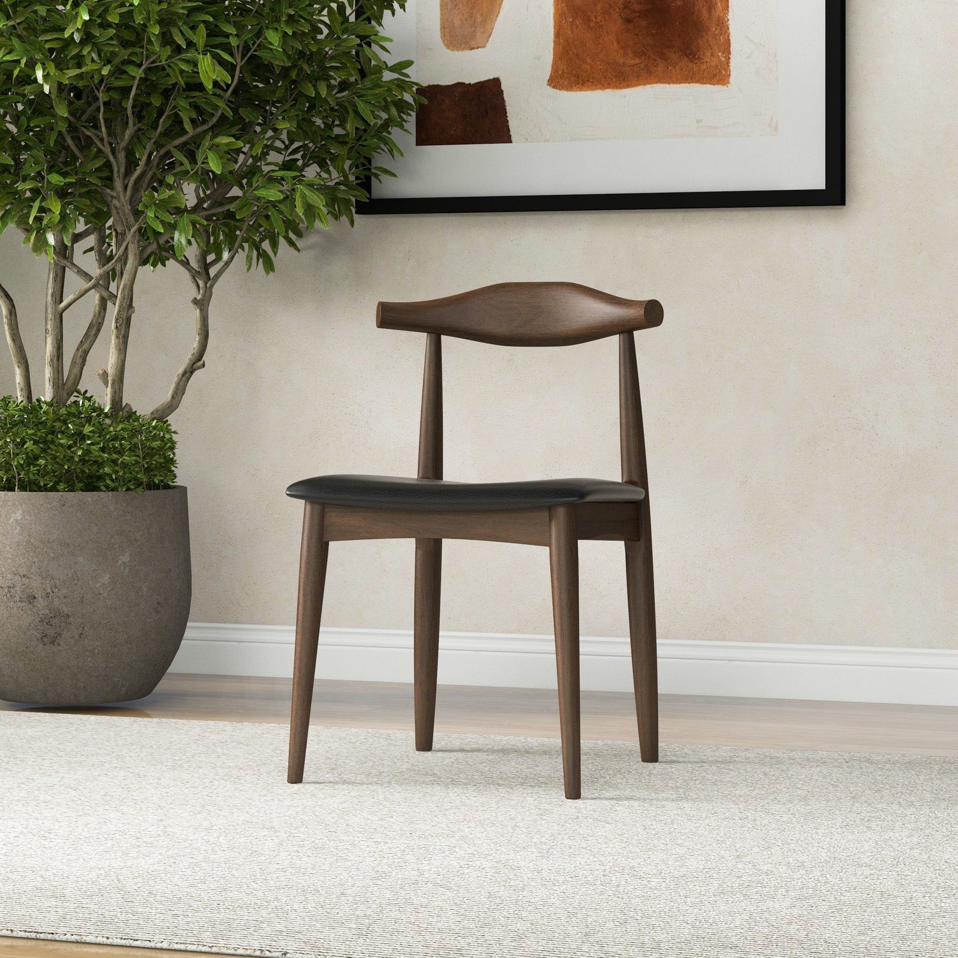 The Destiny - Modern Dining Chairs (Set of 2) feature wooden frames and dark seat cushions, placed on a light carpet by a potted plant. Abstract earthy-toned art hangs behind, complementing the room’s neutral decor.