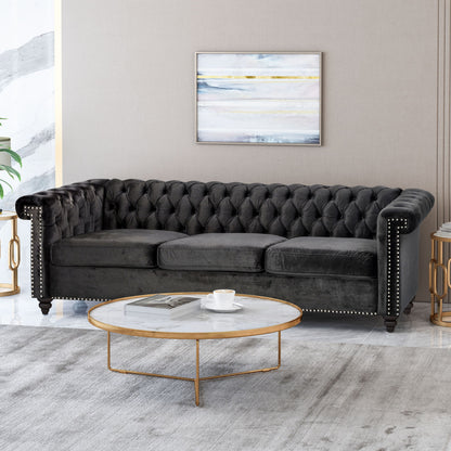 A modern living room features a Chesterfield Style 3 Seater Sofa with deep button tufting, a round marble and gold coffee table with a cup and saucer, a light gray rug, and a framed abstract painting on the wall.