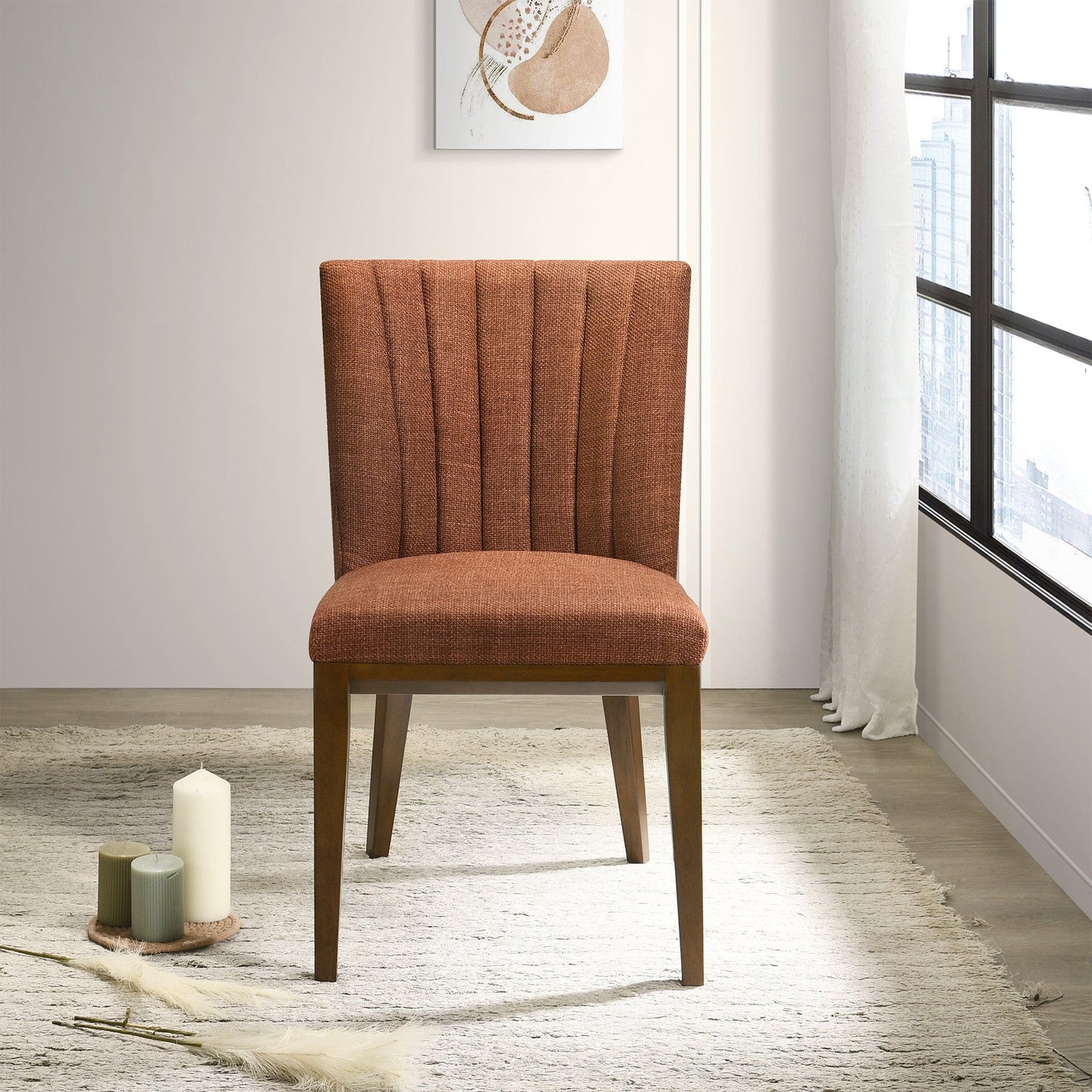 Two Elmwood - Stylish Dining Chairs with wooden legs are placed on a light textured rug by a window. Three decorative candles and a small tray sit nearby, while abstract wall art hangs above, filling the modern room with light.