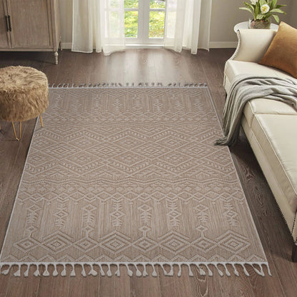 The Guros - Traditional Indoor / Outdoor Area Rug, featuring a beige pattern and tasseled edges, is laid on a dark wood floor in a bright living room with a cream sofa, brown furry ottoman, and sheer white curtains at the window.