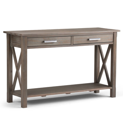 The Kitchener - Handcrafted Table features a weathered wood finish, two front drawers with silver handles, X-shaped side supports, and an open lower shelf.