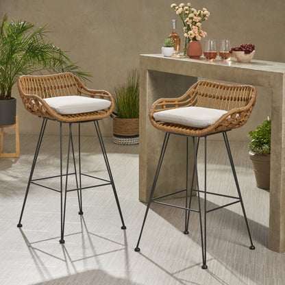 Two Outdoor Rattan Bar Chairs with metal legs and light cushions sit by a stone counter with drinks and flowers, while green potted plants accent the bright, modern indoor space.