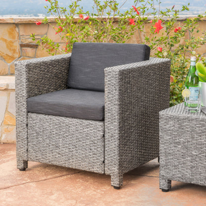 The Stylish Outdoor Club Chair with weather-resistant cushions in gray sits on a stone patio next to a matching table, with glass bottles and flowers displayed in the background.