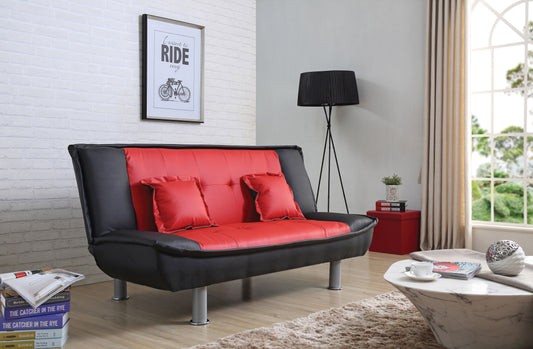 A modern living room features the Lionel Sofa Bed in black and red, paired with two red cushions. A framed picture adorns the white brick wall beside a sleek black lamp. Beige curtains frame a large window letting in natural light, while a marble coffee table with books completes the scene.