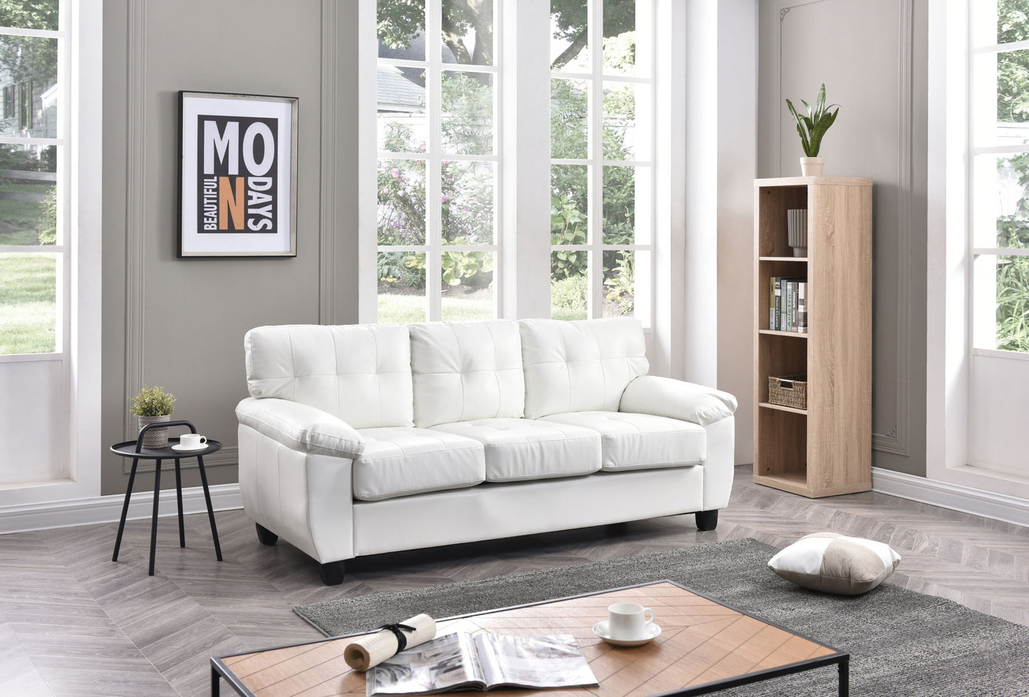 A bright, modern living room with large windows features the Comfortable Sofa in white, a wooden bookshelf with a plant, a side table holding a black cup, and a coffee table displaying an open magazine with a cushion on the floor.