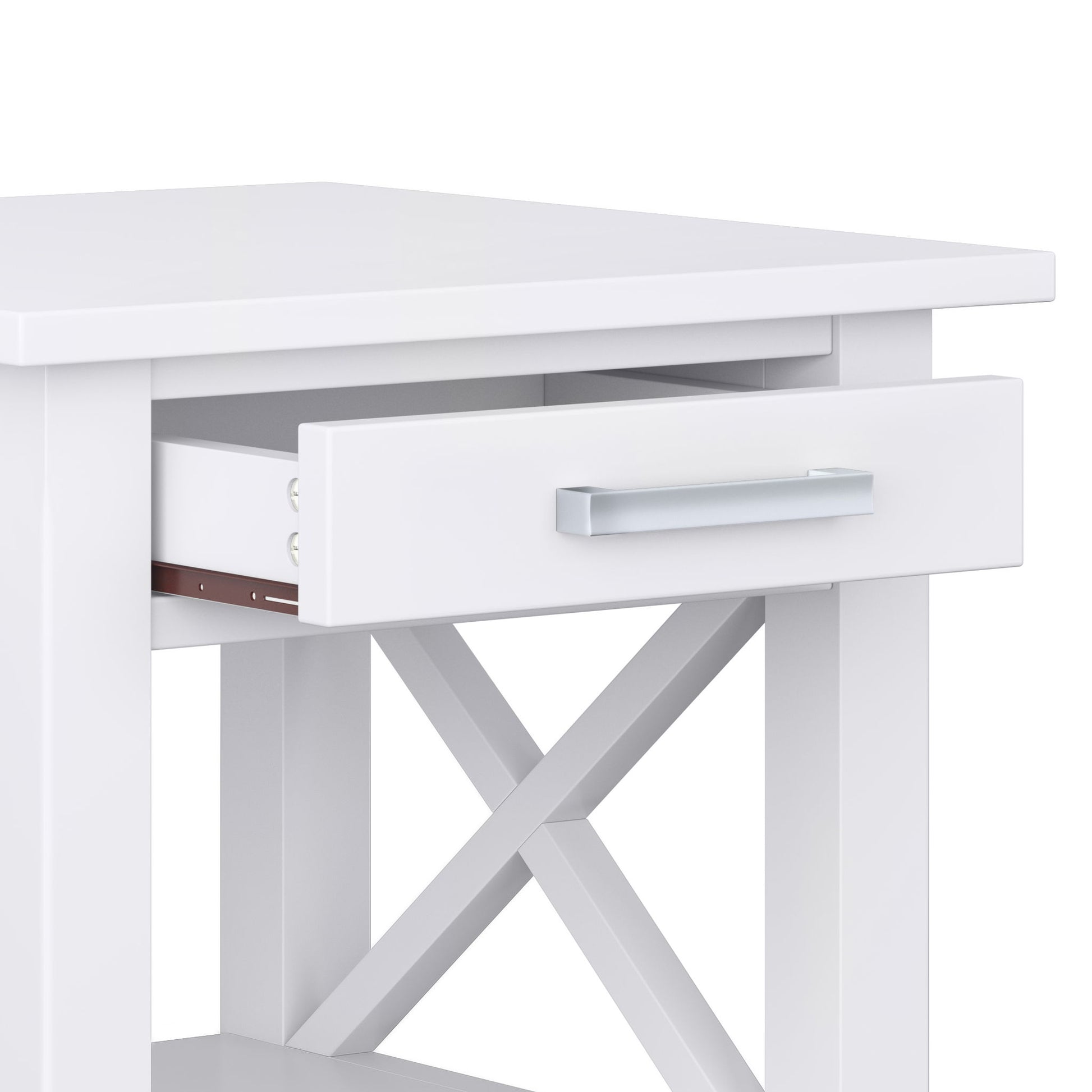 A close-up of the Kitchener - Handcrafted Table, featuring a white finish, open drawer with a silver handle, X-shaped side crossbars for support, a flat tabletop, and an open lower shelf for extra storage.