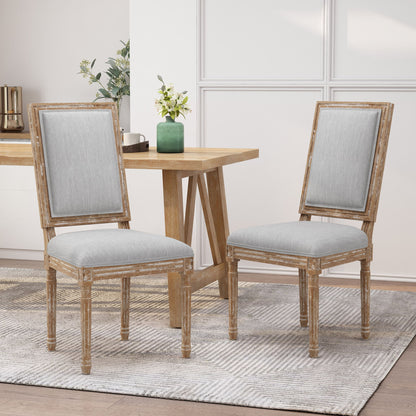 Two French Country Style Dining Chairs with upholstered seats and fluted legs sit on a patterned rug beside a light wood table in a bright, modern room with decorative plants and white paneled walls.