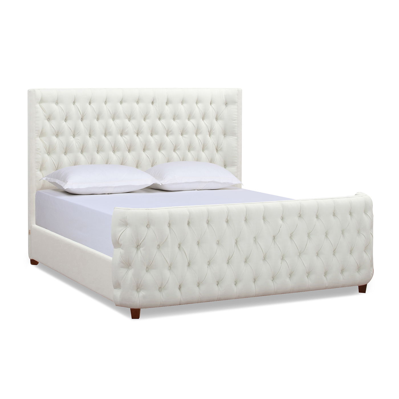 The Brooklyn Tufted Panel Bed features a high headboard and footboard with diamond-pattern button tufting, white upholstery, short wooden legs, and is styled with white pillows and a light gray sheet.