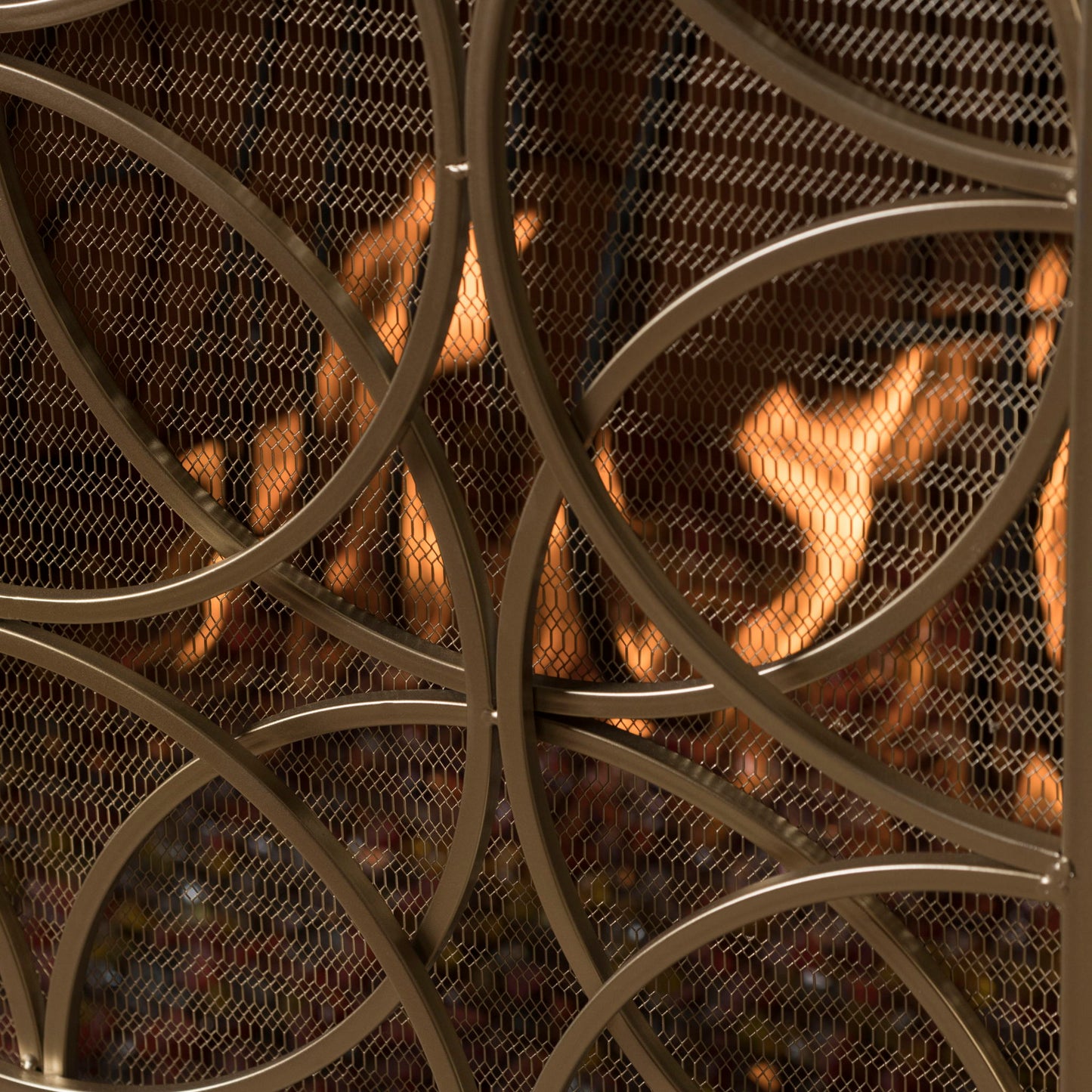 Close-up of the Thayer Single Panel Iron Fireplace Screen featuring a geometric mesh design, positioned in front of a fireplace with visible orange flames in the background.