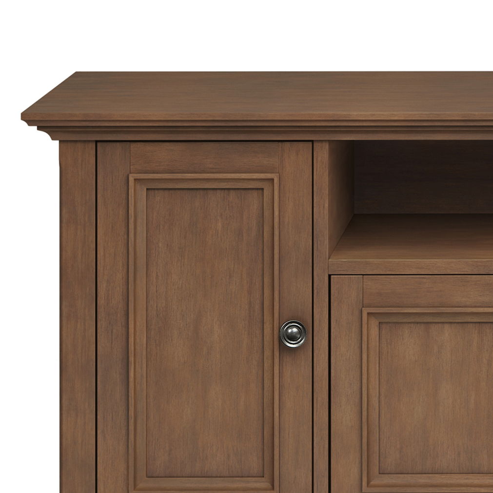 The image shows the Amherst Wide TV Media Stand in Rustic Natural Aged Brown, featuring a panel door with a round metal knob and a rectangular open shelf above, all in a simple, classic design.