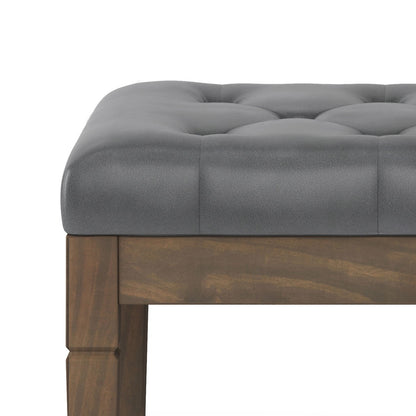 A close-up of the Waverly - Upholstered Tufted Ottoman Bench, featuring a cushioned gray seat and wooden legs, photographed against a white background.