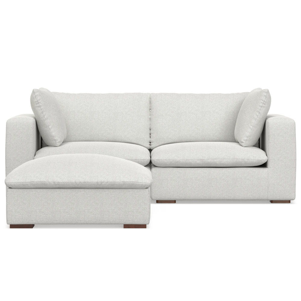 The Jasmine - Handcrafted Sofa And Ottoman is a light gray L-shaped sectional with wide armrests, two back cushions, two side pillows, an extended left chaise for lounging, and short block-style wooden legs.