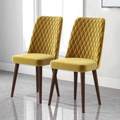 The Katie Mid-Century Modern Dining Chair set of 2 features yellow, diamond-quilted upholstery and wooden legs, shown side by side on a shiny gray floor with natural light from a nearby window.
