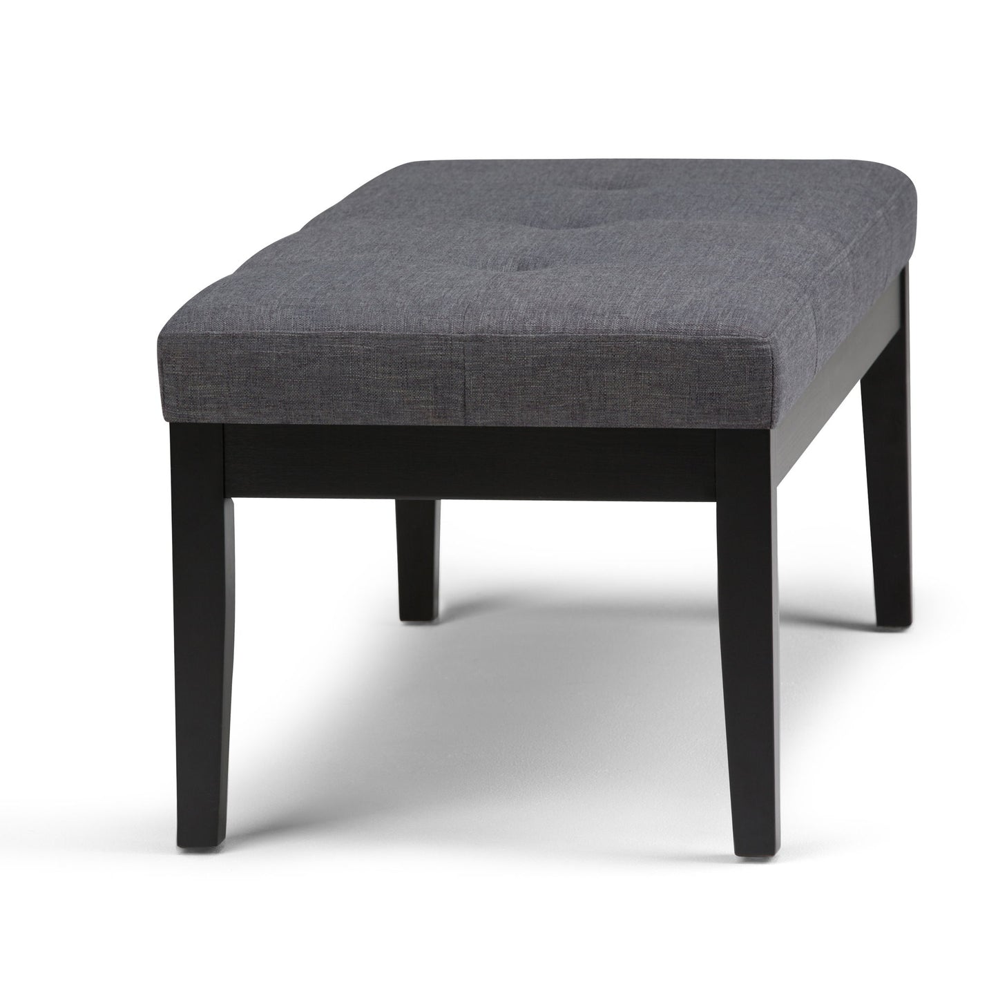 The Lacey Upholstered Tufted Ottoman Bench features a cushioned gray fabric seat with subtle tufted detailing and sturdy black wooden legs.
