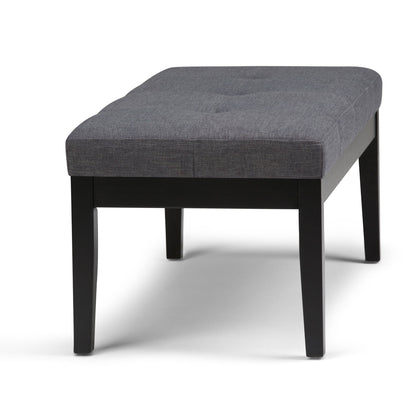 The Lacey Upholstered Tufted Ottoman Bench features a cushioned gray fabric seat with subtle tufted detailing and sturdy black wooden legs.