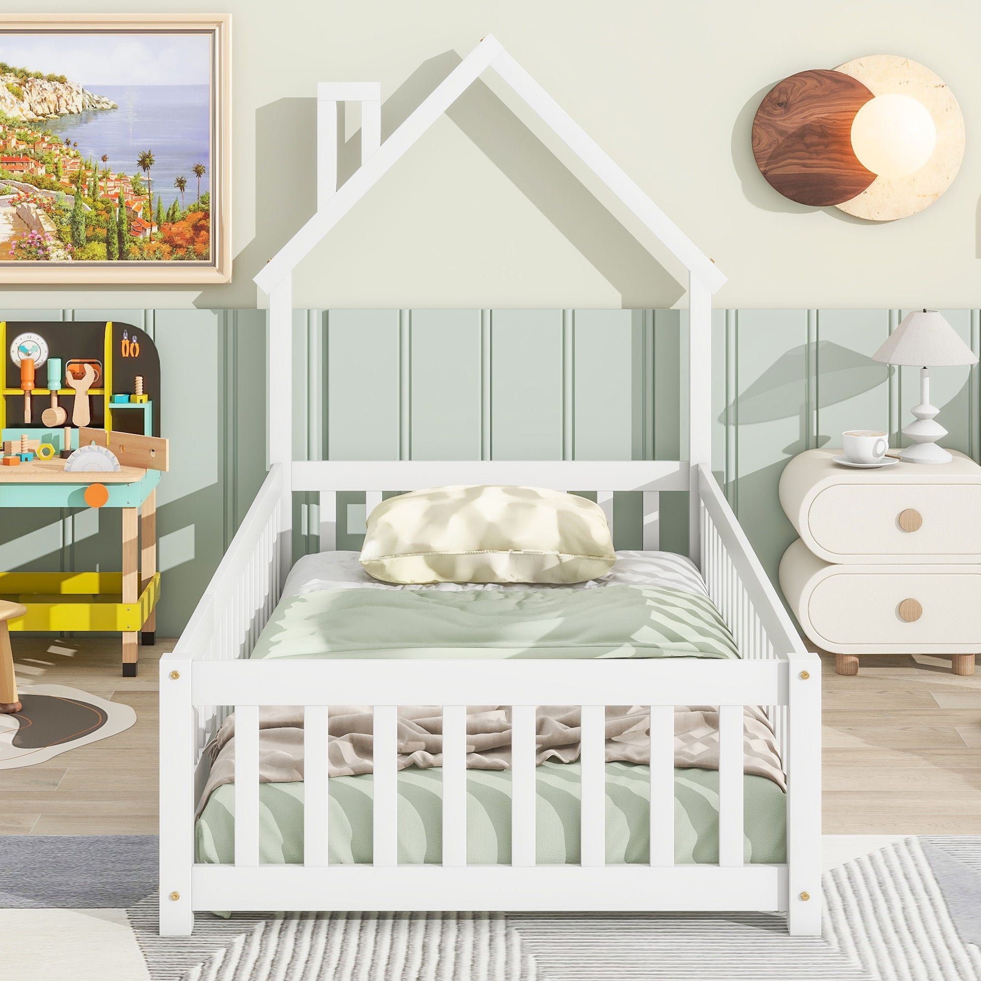 A children's bedroom features a House-Shaped Headboard Floor Bed With Fence in white with green bedding, a pillow, toy workbench, round nightstand and lamp, plus coastal wall art. The room is decorated in soft pastel colors.