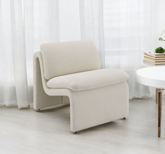 The Jaeda - Innovative Elegance Accent Chair in a modern, curved design rests on a light wood floor by sheer white curtains, accompanied by a round white table and a shelf with books and a plant.