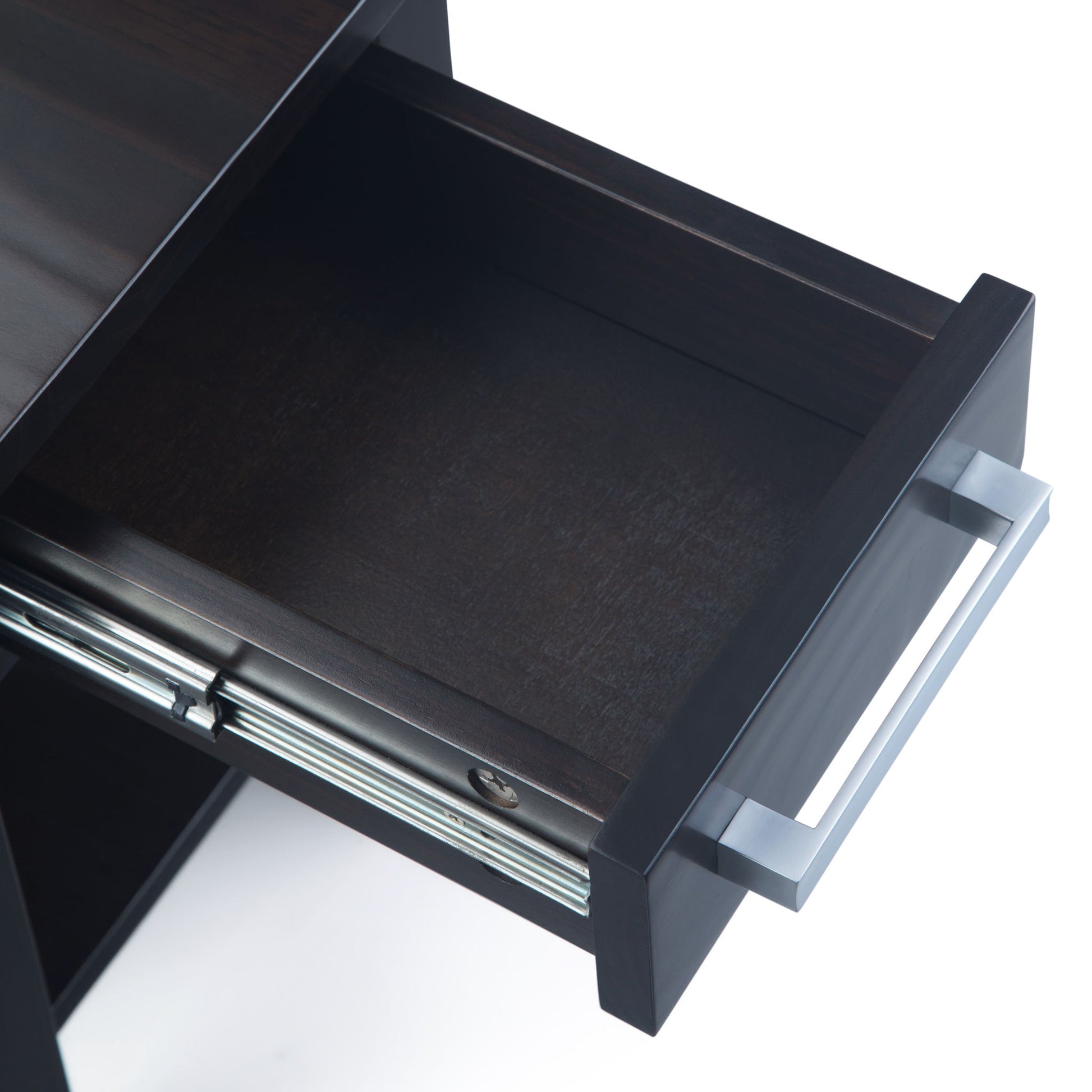 An overhead view of an open, empty dark wood drawer with a silver handle, part of the Kitchener - Handcrafted Table, shown against a white background.