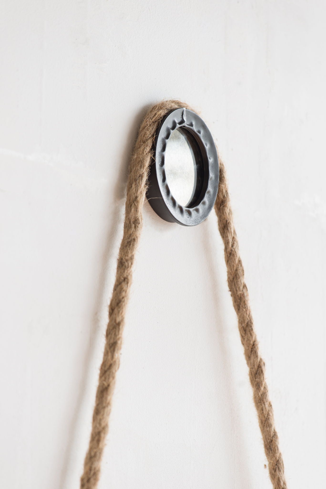 The Handsome Cleveland Mirror features a round metal frame and a thick rope strap for hanging, creating a contemporary look on any plain white wall.