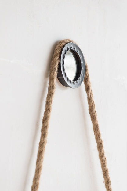 The Handsome Cleveland Mirror features a round metal frame and a thick rope strap for hanging, creating a contemporary look on any plain white wall.
