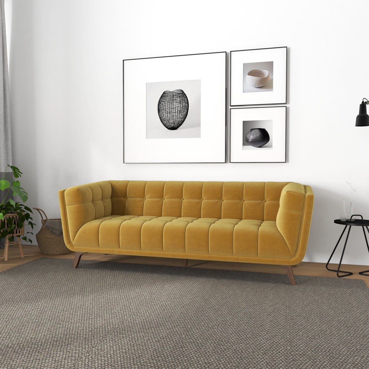 A modern living room featuring the Addison Mid-Century Modern Design Tufted Sofa in mustard yellow, a gray textured rug, minimalist black-and-white wall art, a black floor lamp, small side table, and a potted plant.