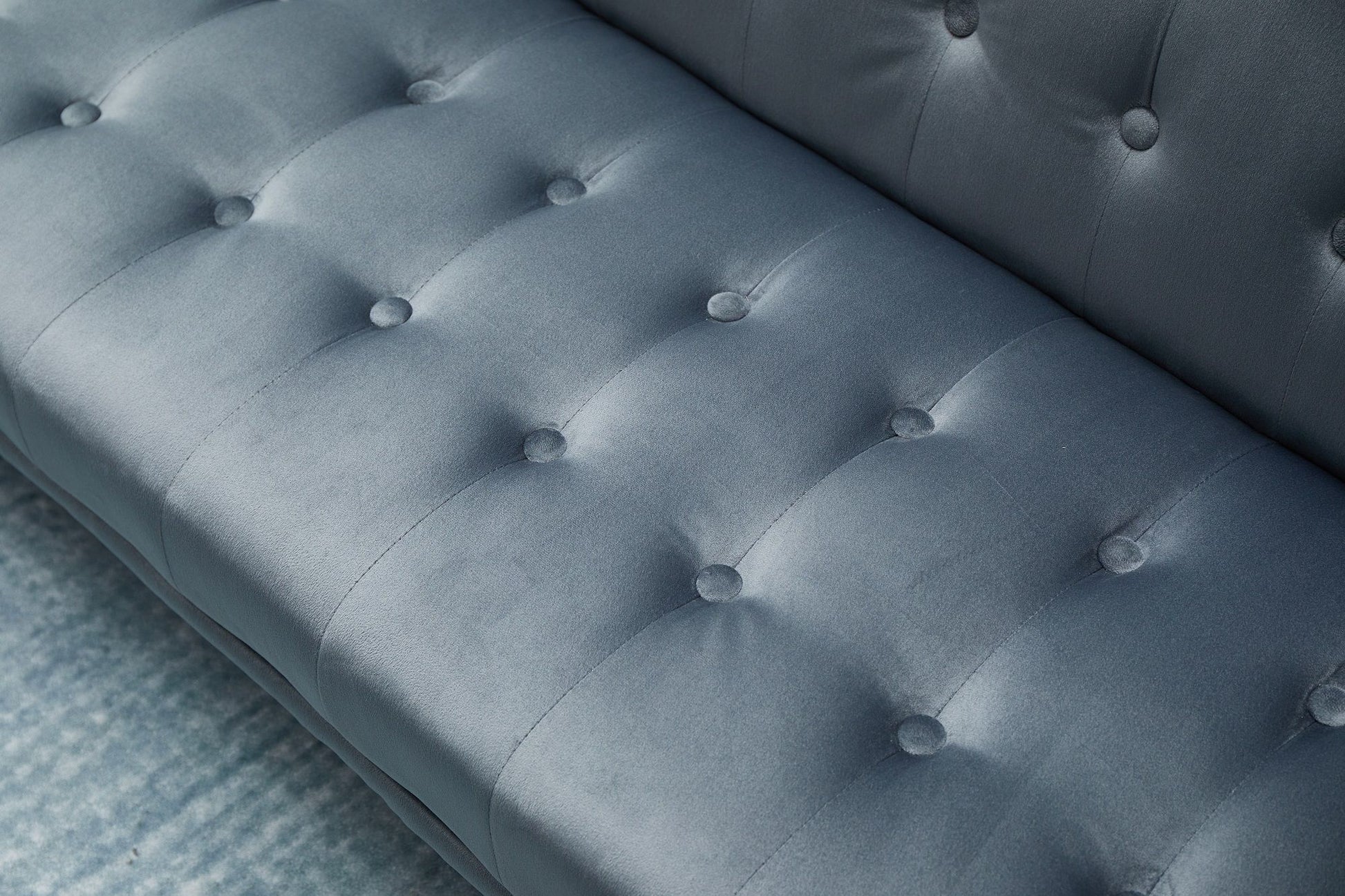 Close-up of the Comfort Compact Design Sofa Bed's blue tufted cushion with button accents and subtle sheen, showing the seat, backrest, and a glimpse of the blue carpet underneath.