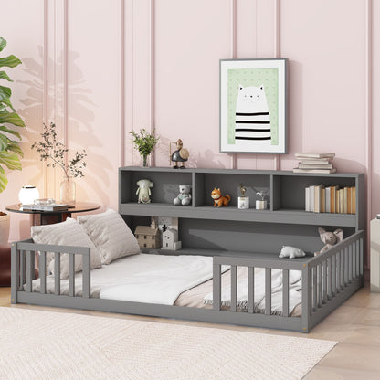 A cozy gray Floor Bed With Side Bookcase, guardrails, and bedding sits against a pink paneled wall. The shelves above display books, toys, and decor. A framed cat print hangs above, with a leafy plant nearby.