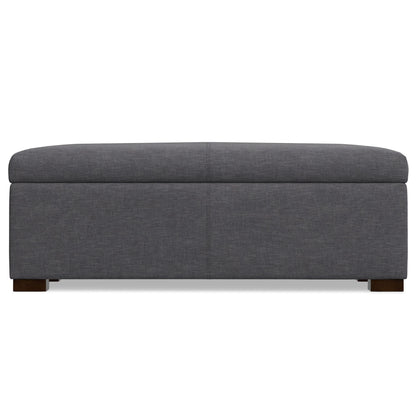 The Gabbie Coffee Table Upholstered Storage Ottoman features a rectangular gray design, hinged lid, and short wooden legs, shown from the front against a white background.
