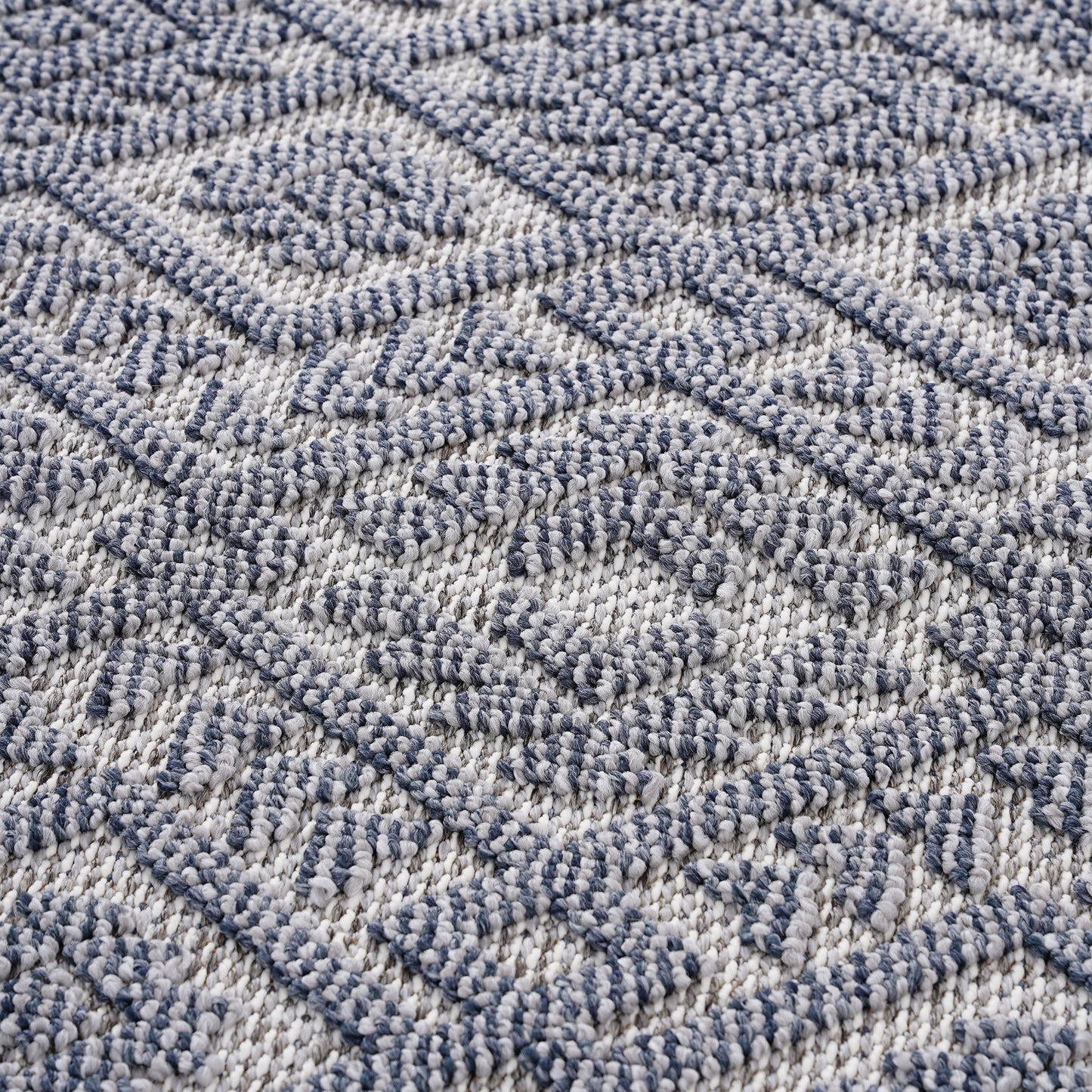 A close-up of the Guros - Traditional Indoor / Outdoor Area Rug, showcasing its blue and white geometric diamond pattern with a textured, slightly raised surface.