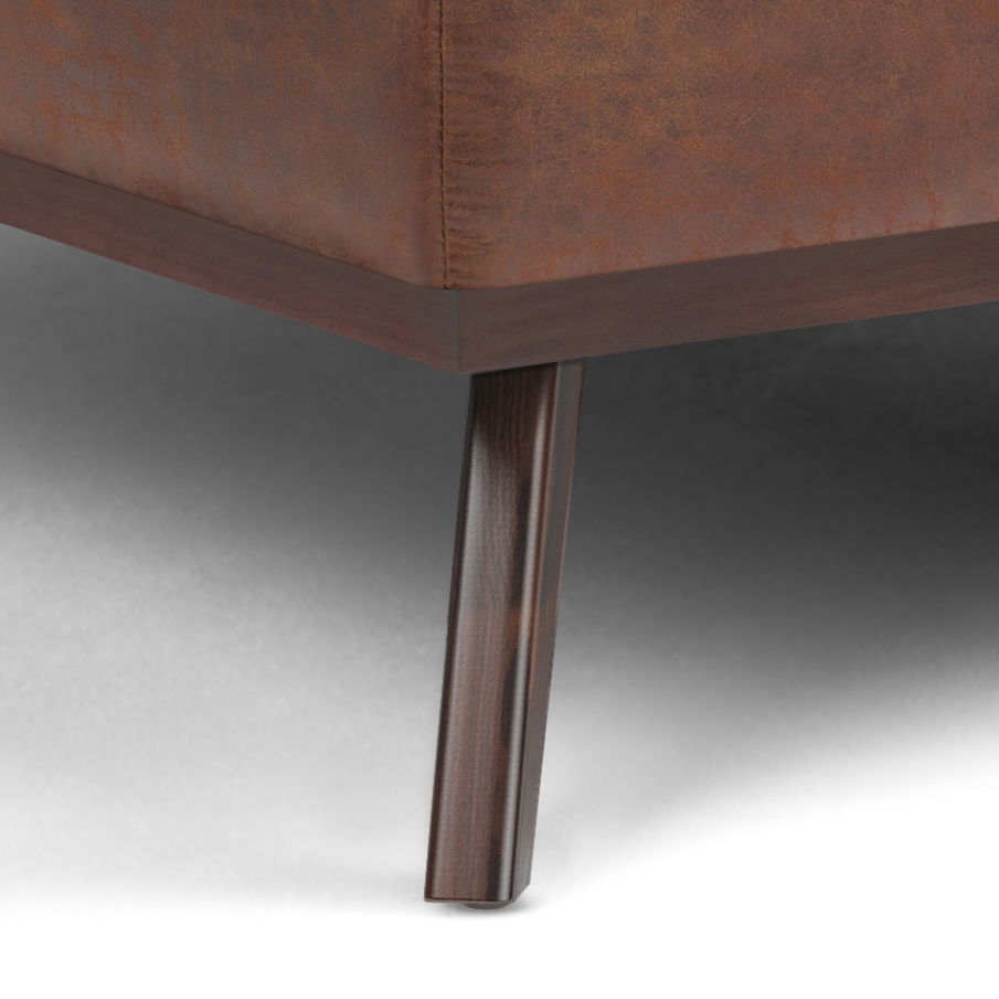 Close-up of the Owen Multifunctional Square Coffee Table Storage Ottoman leg, crafted from dark wood, attached to brown upholstered furniture. The background and floor are light-colored.