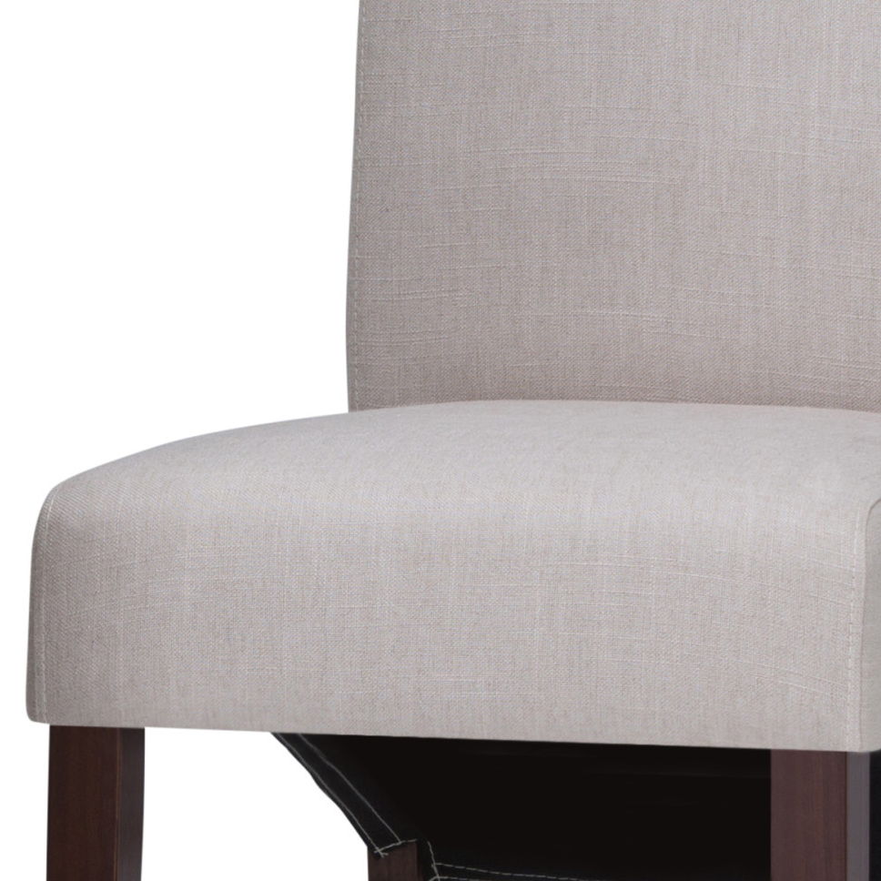 A close-up of the Avalon Deluxe Parson Dining Chair, featuring a light beige upholstered seat and backrest with dark wooden legs, pictured against a white background. Available as a set of 2.