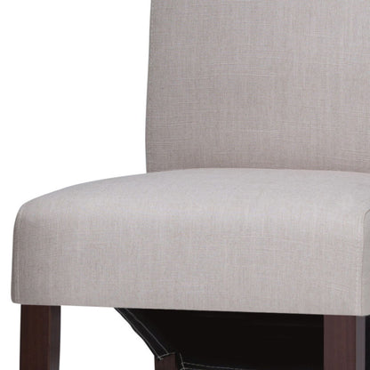 A close-up of the Avalon Deluxe Parson Dining Chair, featuring a light beige upholstered seat and backrest with dark wooden legs, pictured against a white background. Available as a set of 2.