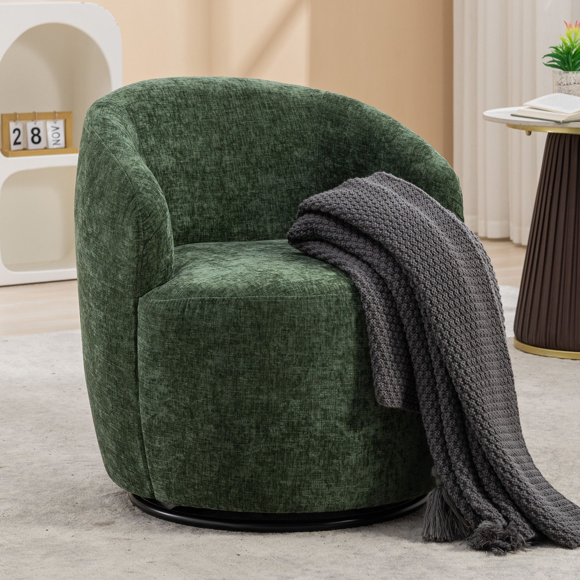 The Chenille Fabric Swivel Accent Armchair Barrel Chair with a curved backrest sits on a light gray rug, draped with a dark gray knitted blanket. A small side table and decorative shelf are visible in the background.
