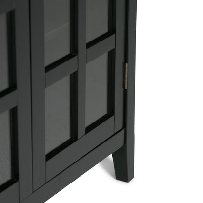 Close-up of the lower corner of the Acadian - Medium Storage Cabinet, Handcrafted; features black glass-paneled doors, a visible metal hinge on the side, and stands on a slightly angled leg.