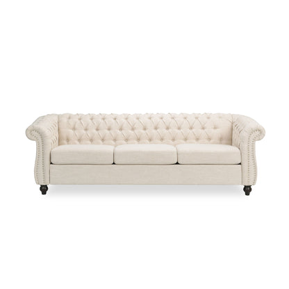 The Chesterfield Style 3 Seater Sofa features cream upholstery, deep button tufting, rolled arms, nailhead trim, and three seat cushions. Shown with short dark wooden legs against a white background.