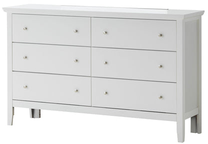 The Primo - Dresser is a white wooden piece with six drawers arranged in two rows of three, each fitted with a small round metal knob. It features clean lines and stands on short legs for a simple, modern look.
