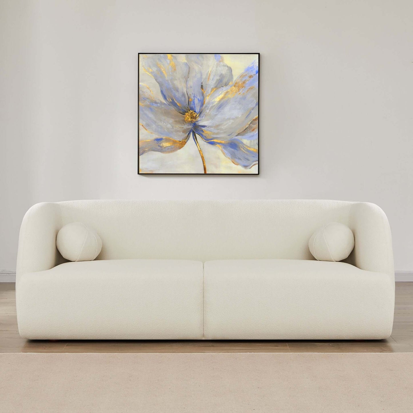 A minimalist living room features the Anna - French Boucle Sofa, topped with two round white cushions, a beige rug underfoot, and a large abstract blue, white, and gold flower painting hanging on the wall above the sofa.