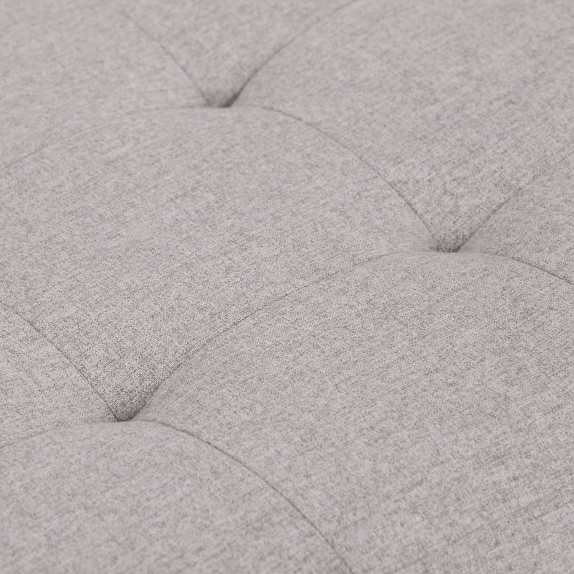 Close-up of the Cosmopolitan Upholstered Storage Ottoman in light gray, highlighting its soft tufted fabric, cushioned texture, and visible stitching with indented seams creating a grid pattern.