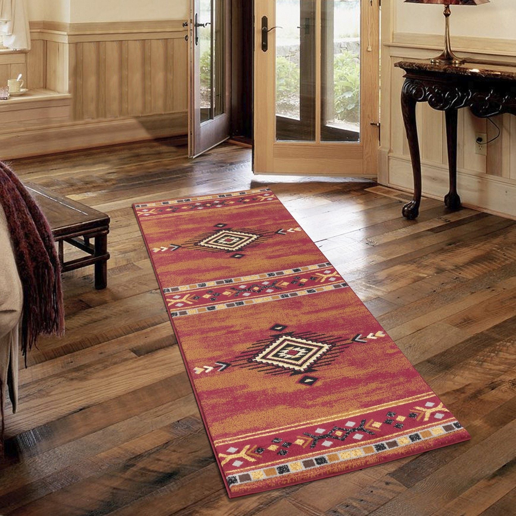 The Tribes - GC_YLS4002 Southwest Area Rug, featuring vibrant geometric patterns, is placed on a wooden floor in a rustic room with wood-paneled walls, a bench, and a dark table beside glass doors to the outdoors.